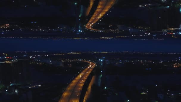 Vista aérea noturna de uma ponte fluvial com carros em movimento e da cidade com luzes noturnas, espelho efeito horizonte. Mídia. Paisagem deslumbrante da cidade noturna e da ponte do outro lado do rio, tema de criação . — Vídeo de Stock