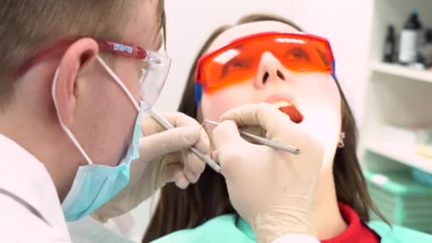 Професійний стоматолог, що працює з пацієнтом у сучасній клініці, концепція медицини. Медіа. Молодий пацієнт в захисних окулярах під час процесу лікування зубів . — стокове відео