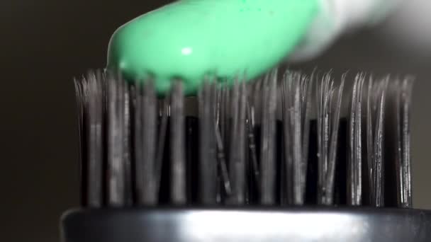 Extrême gros plan d'une brosse à dents grise avec du dentifrice vert pressé du tube sur fond gris foncé, concept de soins dentaires. Media.The soies de la brosse à dents avec du dentifrice frais . — Video