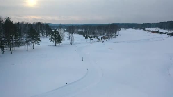 Widok z lotu ptaka toru narciarskiego i ski-domki letniskowe w pobliżu lasu w zimie przed wieczorem szare niebo. Materiał filmowy. Sport i rekreacja — Wideo stockowe