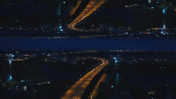 Aerial nattvisning av en river bridge med rörliga bilar och staden med nattlampor, horisont spegeleffekt. Media. Fantastiska landskap av natt stad och bron över floden, starten tema. — Stockfoto