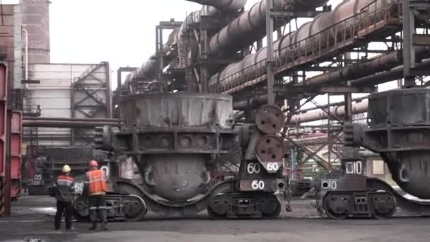 Cubas de fundición de metal que se transportan en carros grandes a la tienda de fundición de metales, concepto de la industria pesada. Dos trabajadores masculinos en uniforme de pie al aire libre en la planta de fundición de metal . — Vídeo de stock