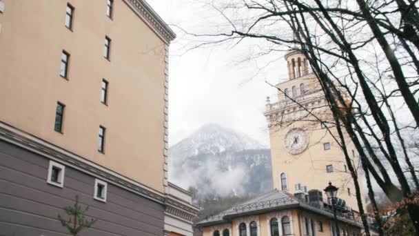 Primer plano de edificios modernos de color beige y gris con altas montañas y árboles en fondo de niebla blanca. Imágenes de archivo. Ciudad cerca de las montañas — Vídeos de Stock