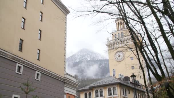 Gros plan des bâtiments modernes beige et gris avec de hautes montagnes et des arbres dans un fond de brouillard blanc. Images d'archives. Ville près des montagnes — Video