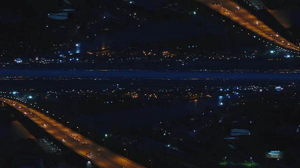 Aerial nattvisning av en river bridge med rörliga bilar och staden med nattlampor, horisont spegeleffekt. Media. Fantastiska landskap av natt stad och bron över floden, starten tema. — Stockfoto