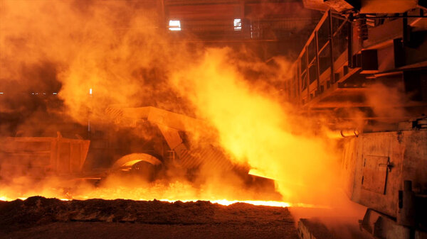 Molten metal flowing in chute at the factory surrounded by steam clubs. Stock footage. Heavy industry and metallurgical plant of steel production.