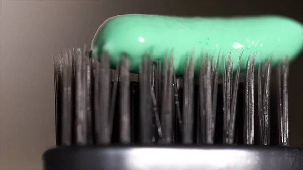 Extreme close up of a grey toothbrush with green toothpaste being squeeezed from the tube on dark grey background, dental care concept. Media.The щетина зубной щетки со свежей зубной пастой . — стоковое фото