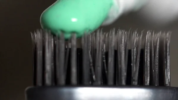 Extreme close up of a grey toothbrush with green toothpaste being squeeezed from the tube on dark grey background, dental care concept. Media.The щетина зубной щетки со свежей зубной пастой . — стоковое фото