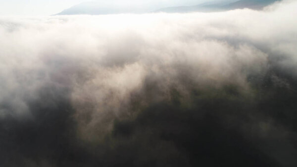 Вид с воздуха на облака и пейзаж под ними. Выстрел. Верхний вид облаков под небом. Под облаками, сбитыми с птичьего полета, светит солнце на облаках
