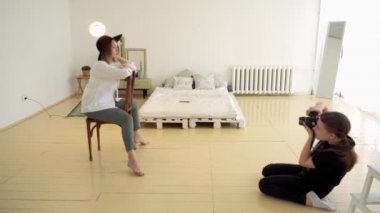 Kadın fotoğrafçı, sandalyede oturan kadın modelinin profesyonel fotoğraflarını çeker. Medya. Çekici kadın fotoğrafçı ve model yatak ile uyku iç stüdyoda çalışan