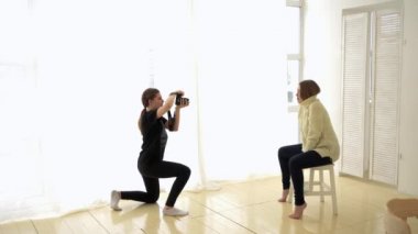 Çekim öncesi kadın fotoğrafçı ve model. Medya. Fotoğrafçı daha iyi çekim almak için model ile etkileşime girer. Pencere aydınlatma tarafından sandalyeye oturan kadın romantik çekim