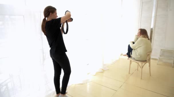 Ο φωτογράφος παίρνει το μοντέλο καθισμένος στην καρέκλα. Media. Το μοντέλο είναι ρομαντικά τοποθετημένο στην καρέκλα κοντά στο παράθυρο του ήπιων φωτός, δουλεύοντας με επαγγελματία φωτογράφο — Αρχείο Βίντεο