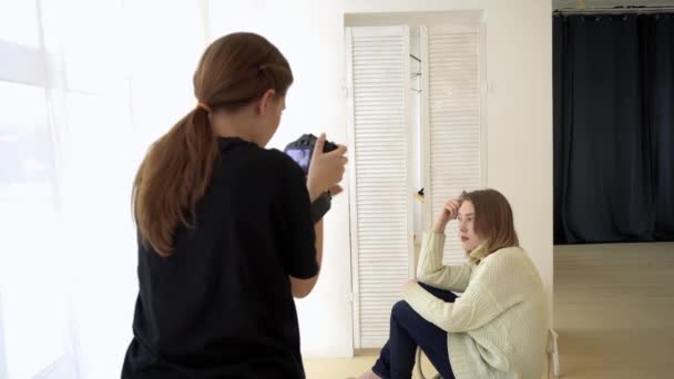 Woman photographer and model before shooting. Media. Photographer interacts with model to get better shot. Romantic shooting of woman sitting on chair by window lighting — Stock Video