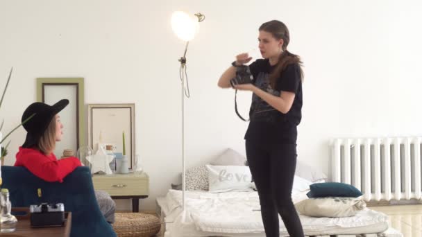 Vrouw is fotograaf en model tijdens het fotograferen. Media. Fotograaf rechtzetten zijn hoed op aantrekkelijke vrouwelijke model zittend in de stoel voor het fotograferen in Photo Studio — Stockvideo