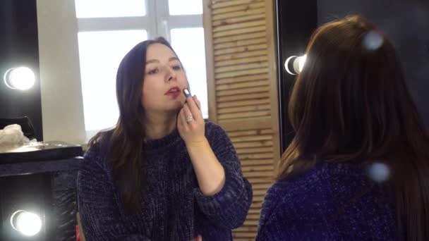 Young woman paints lips in photo studio. Media. Woman fixing make-up tinting lips in mirror with light bulbs. Dressing room in photo studio — Stock Video