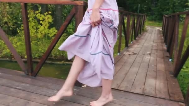 川の近くの木製の桟橋を歩く軽いスカートのかわいい若い女性の足のクローズアップ。カントリーウォーク. — ストック動画