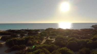 Güzel plaj mavi deniz ve gökyüzü arka planda çalılar ile büyümüş. Madde. Açık gökyüzü ile ufuk için denizin mavi yüzeyinde Güneş dalgalar