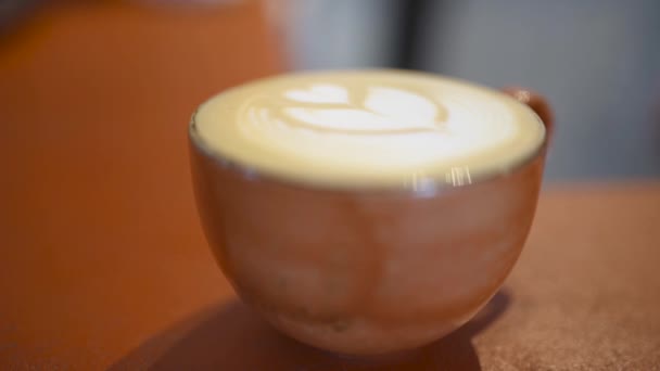 コフェとパターンでカップのクローズアップ。第。クリームのハートパターンと居心地の良い香りのカフェマグカップは、カフェのテーブルの上にあります — ストック動画