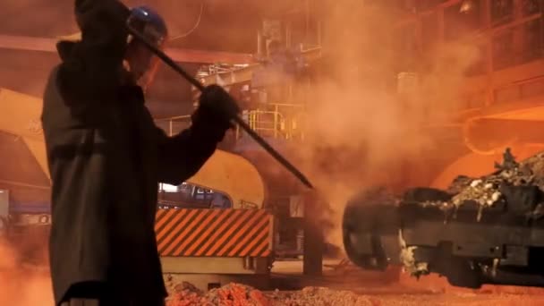 Furnace man in protective unifom cleaning pipe with a poker. Stock footage. Worker preparing equipment after steel production in an electric furnace. — Stock Video