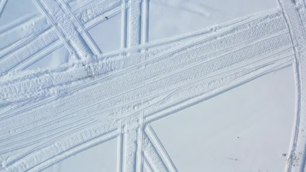 Вид сверху на катание на снегоходах. Запись. Вид сверху на два снегохода, едущих по кругу, оставляя следы на снегу в солнечный день — стоковое видео
