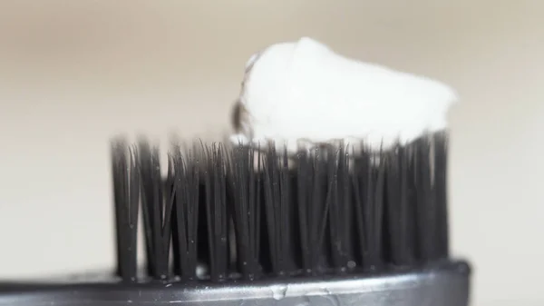 Extreme close-up voor een zwarte tandenborstel met witte tandpasta wordt geperst op het op beige achtergrond. Media. De zwarte haren van de tandenborstel met witte tandpasta, tandheelkundige zorgconcept. — Stockfoto