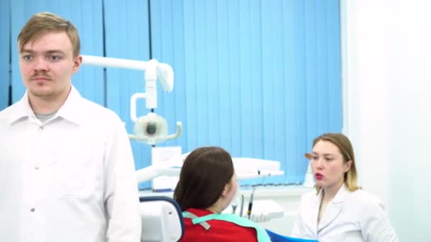 O médico está se preparando para o próximo procedimento e colocando máscara protetora com seu assistente conversando com o paciente. Mídia. Jovens médicos no trabalho na clínica odontológica, conceito de medicina . — Vídeo de Stock