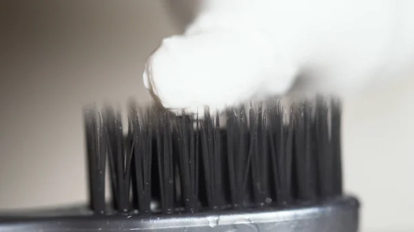 Extreme close-up voor een zwarte tandenborstel met witte tandpasta wordt geperst op het op beige achtergrond. Media. De zwarte haren van de tandenborstel met witte tandpasta, tandheelkundige zorgconcept. — Stockfoto