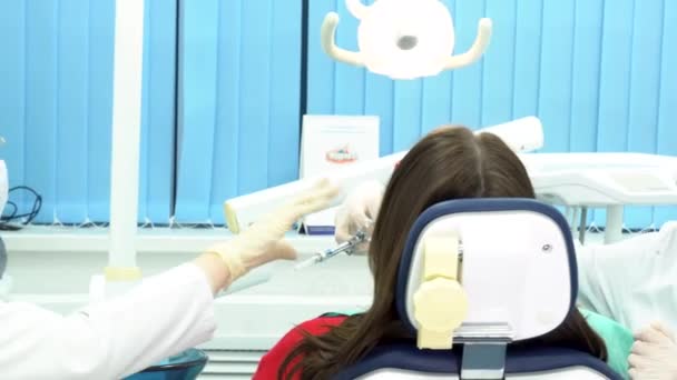 Вид сзади на пациентку, сидящую в стоматологическом кресле и получающую укол у стоматолога. СМИ. Дантист и ее ассистент делают инъекцию женщине перед медицинской процедурой . — стоковое видео