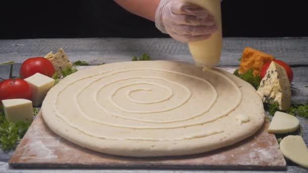 Close-up de mãos de chefs cobrindo a massa de pizza com molho branco em uma tábua de madeira com ingredientes diferentes. Moldura. Deliciosa preparação de pizza — Vídeo de Stock