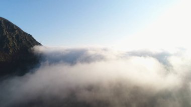 Mavi gökyüzü ve parlak güneşe karşı bulutlar yoğun tabakası ile çevrili yüksek dağ üst güzel görünümü. Atış. Dağ manzarası