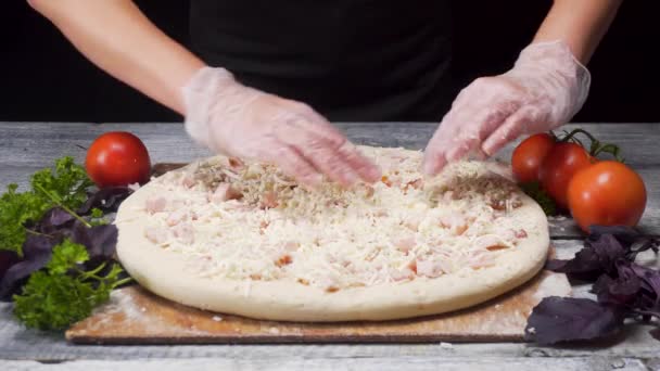Zavřete ruce v rukavicích, které připravují pizzu ležící na dřevěné desce s čerstvou zeleninou a konceptem pro potravinářství. Rámeček. Šéfkuchař dělá pizzu na stole na černém pozadí. — Stock video