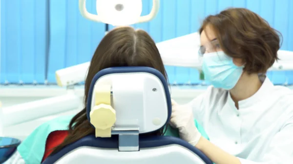 Rear view of female patient sitting in dental chair receiving an injection at the dentist. Media. Dentist woman making an injection to a female patient before medical procedure.