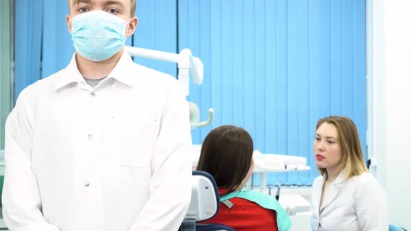 De arts bereidt zich voor op de aankomende procedure en zet het beschermende masker met zijn assistent praten met de patiënt. Media. Young Doctors aan het werk bij Dental Clinic, Medicine concept. — Stockfoto