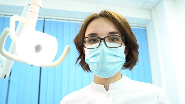 Punto de vista del paciente de un dentista que examina la boca del paciente, concepto de odontología moderna. Medios. Joven dentista mirando a la paciente y girando la lámpara . —  Fotos de Stock