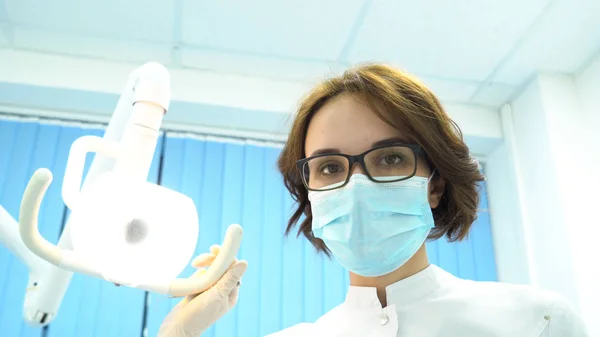 Eerste persoon weergave van een jonge vrouwelijke tandarts in masker benaderingen met gereedschap. Media. Jonge arts staande over de patiënt, kijken naar camera. — Stockfoto