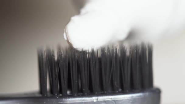 Extremo acercamiento para un cepillo de dientes negro con pasta de dientes blanca que se aprieta sobre él sobre fondo beige. Medios. Las cerdas negras del cepillo de dientes con pasta de dientes blanca, concepto de cuidado dental . — Vídeo de stock