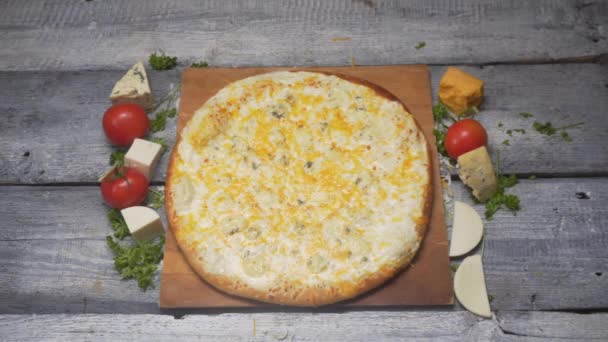 Крупный план вкусной свежей итальянской пиццы с четырьмя сырами на деревянной доске с кусочками помидоров и сыра на сером деревянном столе. Рамка. Итальянская кухня — стоковое видео