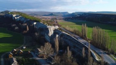 Çarpıcı doğal taş duvar, büyüyen ağaçlar ve her iki tarafında yeşil alanlar ile yüksek ve uzun uçurum havadan görünümü. Atış. Yüksek dağlar ve vadide bir köy ile güzel manzara.
