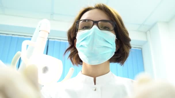 Вид от первого лица молодой женщины-стоматолога в маске подходит с инструментами. СМИ. Молодой доктор стоит над пациентом, смотрит в камеру . — стоковое видео
