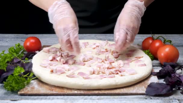 Cook na stawia kiełbasa na pizzę. Ramki. Szef kuchni w pizzerii ubrany w rękawice stawia warstwę mięsa na pizzę otoczoną składnikami na czarnym tle — Wideo stockowe
