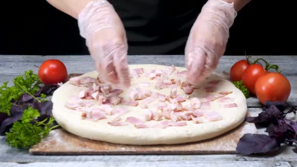 Cook på sätter korv på pizza. Ram. i pizzeria bär handskar sätter kött lager på pizza omgiven av ingredienser på svart bakgrund — Stockvideo