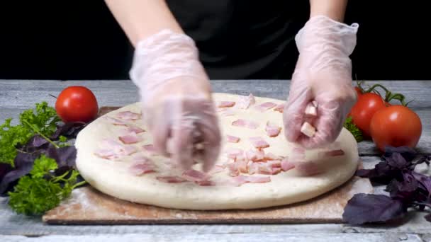 Cook on puts sausage on pizza. Frame. Chef in pizzeria wearing gloves puts meat layer on pizza surrounded by ingredients on black background — Stock Video
