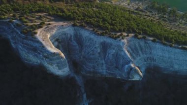 Yeşil alan ve küçük evlerin yakınında iğne yapraklı ağaçlarla kaplı yüksek gri dağ uçurumun havadan görünümü. Görüntü. Güzel yaz manzara
