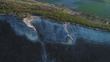 Yeşil alan ve küçük evlerin yakınında iğne yapraklı ağaçlarla kaplı yüksek gri dağ uçurumun havadan görünümü. Görüntü. Güzel yaz manzara