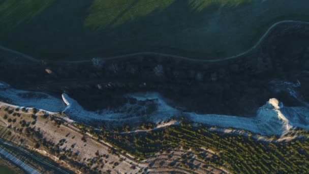 Top view of the mountain cliff covered with coniferous trees between the green field and highway. Footage. Beautiful summer landscape — Stock Video