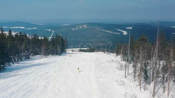 Hermosa vista aérea de las personas en una pista de esquí que comienza a esquiar por una pista cerca de árboles de coníferas y teleférico contra el cielo azul nublado. Filmación. Estación de esquí — Vídeos de Stock