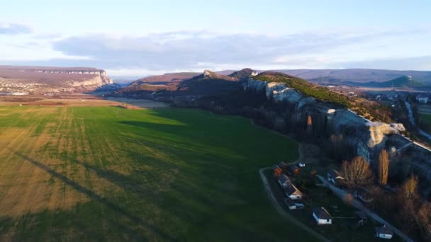 Vista superior del paisaje de montaña con campos verdes bajo el sol de la noche. Le dispararon. Hermosa zona de montaña con roca de piedra verde exuberante campo al pie del horizonte de montaña con cielo nublado — Vídeo de stock