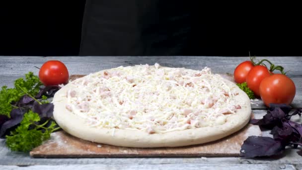 Pizza crua com presunto e queijo. Moldura. Massa polvilhada com queijo para pizza, cercada por ingredientes antes de cozinhar e assar em fundo preto — Vídeo de Stock