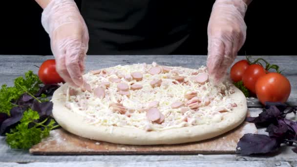 Cucini su mette la salsiccia a pizza. Cornice. Lo chef in pizzeria indossando i guanti mette lo strato di carne sulla pizza circondato da ingredienti su fondo nero — Video Stock