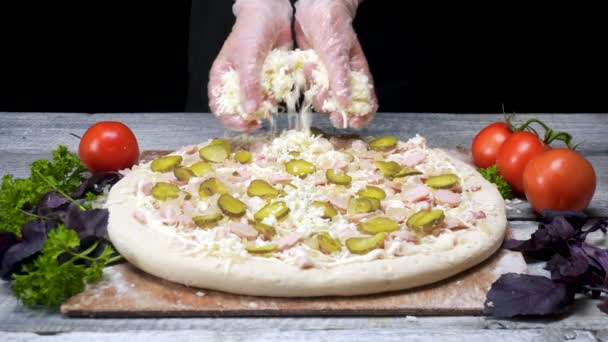 Lo chef spruzza pizza con formaggio grattugiato. Cornice. Professionale pizzeria chef in guanti mette ultimo strato di formaggio su sfondo nero — Video Stock